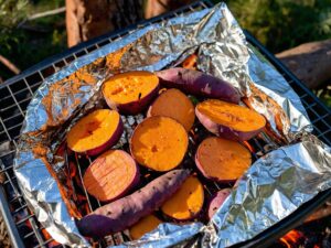 Foil-wrapped sweet potatoes cooking on a campfire grill