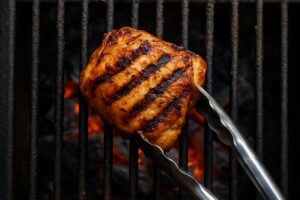 flipping grilled chicken thigh with tongs